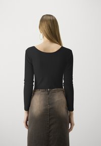 Top a maniche lunghe nero a costine abbinato a una gonna di jeans marrone aderente con zip centrale e superficie liscia e texture.