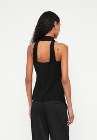 Črna top s trakovi za vrh vratu z teksturirano površino, odprtim hrbtnim delom in širokimi trakovi. Nošeno s črnimi, širokimi hlačami.