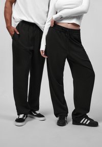 Pantalons noirs à rayures avec une coupe ample et une taille élastique, portés avec des hauts à manches longues blancs contrastants et différents styles de baskets.