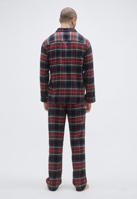 Czerwono-czarny flanelowy komplet piżamowy z guzikiem na górze i długimi spodniami, charakteryzujący się luźnym krojem i miękkim materiałem. Widok od tyłu.