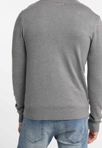 Maglione grigio a maglia con orlo e polsini a coste, design aderente e texture liscia, abbinato a jeans blu in vestibilità rilassata.