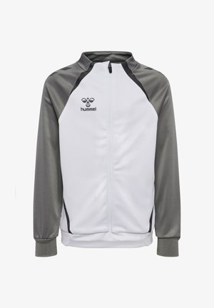 To børn iført matchende hvide og grå Hummel-træningsdragter står side om side mod en ensfarvet baggrund.