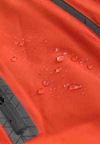 Tessuto arancione resistente all'acqua con gocce sulla superficie. Presenta una zip nera e un accento testurizzato vicino al fondo.