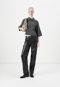 Kort gesneden grijze spijkerblouse met korte mouwen, voorzak; zwarte faux leren wijde broek; handtas met slangenprint; chunky haklaarzen.