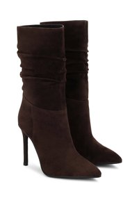 Botas altas de tacón de ante marrón con puntera afilada y diseño superior fruncido, que presentan una textura suave y una silueta elegante.