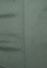 Närbild av grönt tyg med en vertikal söm som löper ner genom mitten, vilket visar fin textur och sömnadsdetaljer.