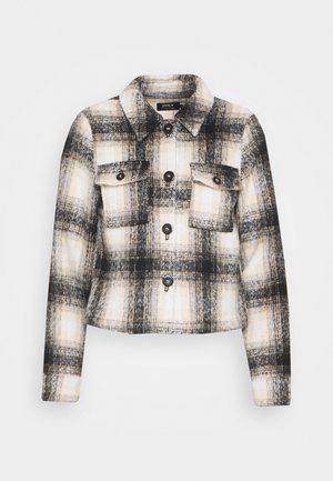 Cropped flannel jacket in beige, black, and white plaid pattern. Features two chest pockets, button closures, and a classic collar design.