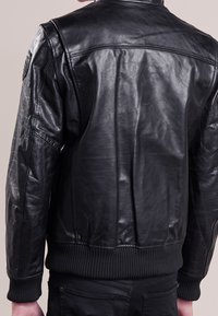 Veste bomber en cuir noir avec des poignets et un ourlet côtelés, présentant une texture lisse et un design classique, avec des détails de couture visibles à l'arrière.