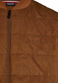 Braune Wildleder-Bomberjacke mit Reißverschluss, geripptem Kragen und geprägtem Logo. Vertikale Nähte sorgen für Textur und Details.