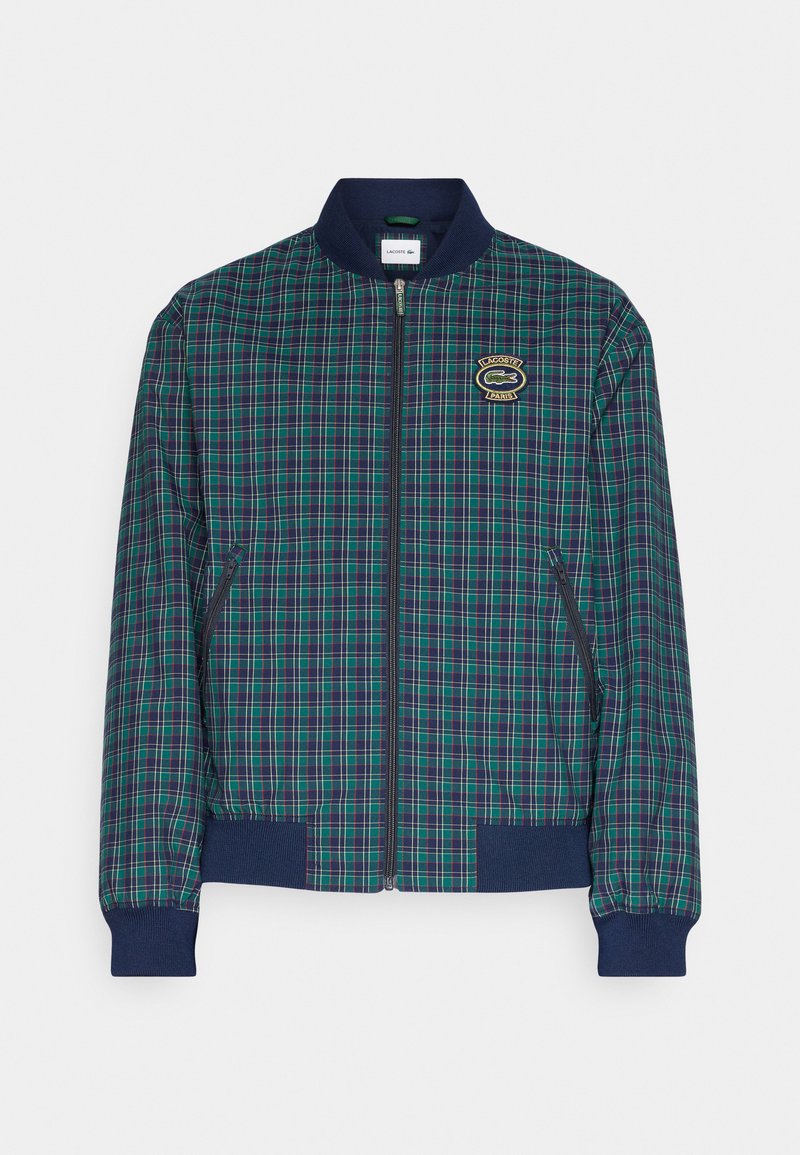 Veste bomber à carreaux bleu marine et vert avec fermeture éclair, poignets côtelés et patch logo Lacoste sur la poitrine gauche. Matériau léger.