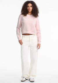 Light pink cropped sweatshirt with embroidered logo, paired with loose-fitting, white cargo pants featuring side pockets, and white sneakers.