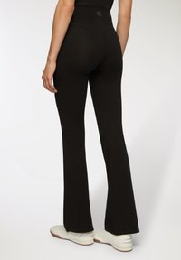 Leggings neri a campana con vita alta, realizzati in un materiale elastico. Presentano un piccolo logo sulla fascia posteriore e una superficie liscia.