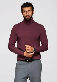 Burgundyröd polokrage tröja i slät tyg, med långa ärmar och en kroppsnära design, tillsammans med grå byxor och ett svart bälte.