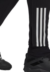 Zwarte sportbroek met drie witte verticale strepen en zijritsen, gecombineerd met zwarte high-top sneakers met een gestructureerd ontwerp.