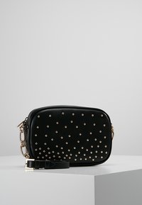 Černá taška z umělé kůže se zlatými cvočky, obdélníkového tvaru, se zipovým uzávěrem a nastavitelným popruhem. Obsahuje řetízkový akcent.