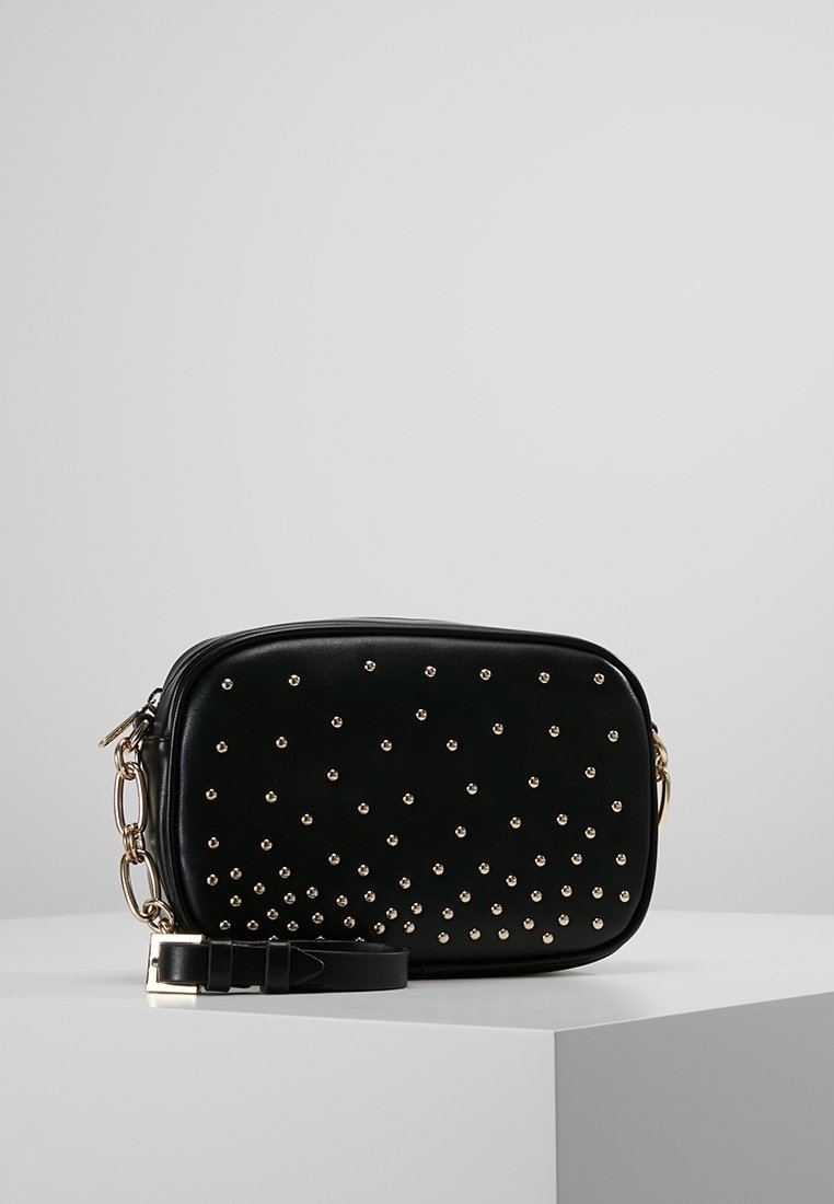 Černá taška z umělé kůže se zlatými cvočky, obdélníkového tvaru, se zipovým uzávěrem a nastavitelným popruhem. Obsahuje řetízkový akcent.