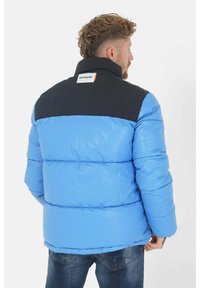Gevoerde jas met een glanzende textuur, met een lichtblauwe body en een zwarte bovenkant. Inclusief een label op de achterkant en een hoge kraag.