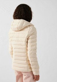 Gevoerde crèmekleurige jas met een afneembare capuchon, voorzien van horizontale stiknaden, lange mouwen en een getailleerd ontwerp.