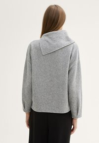 Grauer Strickpullover mit großem Kragen, überschnittenen Schultern und langen Ärmeln. Weiche Textur und cropped Design. Die Rückansicht zeigt eine schlichte Silhouette.