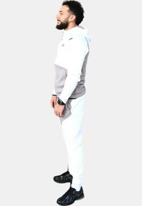 Conjunto atlético para hombre que incluye una sudadera blanca con detalles en gris, pantalones blancos a juego y zapatillas negras. Textura de tela suave, diseño deportivo.