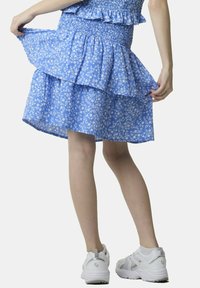 Gonna tiered blu con stampa floreale, con vita arricciata, realizzata in tessuto leggero. Abbinata a scarpe sportive bianche con un design testurizzato.
