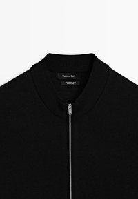 Sort merinould zip-up sweater med ribbet hals og sølv lynlåsdetaljer. Mærke synligt på den indvendige krave.
