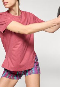 Punainen urheilu T-paita lyhyillä hihoilla, yhdistettynä kirkkaan violettiin ja turkoosiin kuvioituun shortsipariin, joissa on Puma-logo.