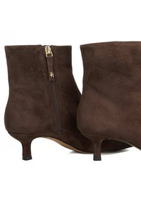 Bottines en suède marron avec une fermeture éclair sur le côté, dotées d'un petit talon et d'une finition lisse et texturée. Design élégant avec des accents minimalistes.