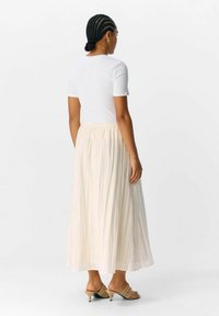 Top blanco de manga corta combinado con una falda maxi plisada color crema. La falda tiene una textura suave, cintura elástica y se lleva con tacones de color marrón claro.