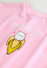 Tricou roz din bumbac, cu text brodat alb "bananya" și un desen animat cu o pisică stând pe o banană galbenă, cu un detaliu în formă de inimă roz.