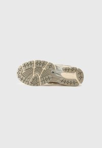 Shoe outsole in beige and gray with textured rubber tread patterns, grooves, and a reinforced midsole for stability and traction.