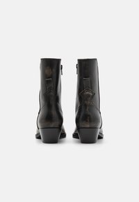 Bottes de cheville en cuir noir avec une finition lisse, un talon empilé, des fermetures éclair sur le côté et des coutures décoratives sur le panneau arrière.