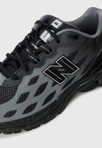 Baskets de course noires et grises avec une tige en maille, des découpes angulaires, une semelle épaisse et un logo bien en vue sur le côté. Lacets texturés et accents inclus.