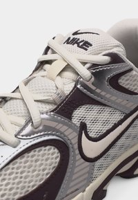 Baskets Nike blanches et violet foncé en tissu mesh, avec des superpositions argentées et des lacets blancs noués, affichant le logo Nike sur le côté et la languette.