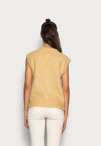 Sweter z krótkim rękawem z miękkiego, żółtego dziania. Ma wykończenie ze ściągaczem u dołu i lekko postrzępione krawędzie. Połączony z białymi dopasowanymi spodniami.