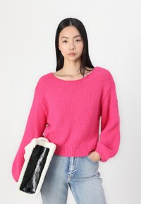 Chunky pink knit sweater with a wide neckline and voluminous sleeves, paired with a black and white fur-textured rectangular clutch.