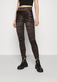Leggings en satin marron avec un design froncé, une taille haute et une coupe ajustée. Associez-les à des bottines à plateforme noires pour un contraste.