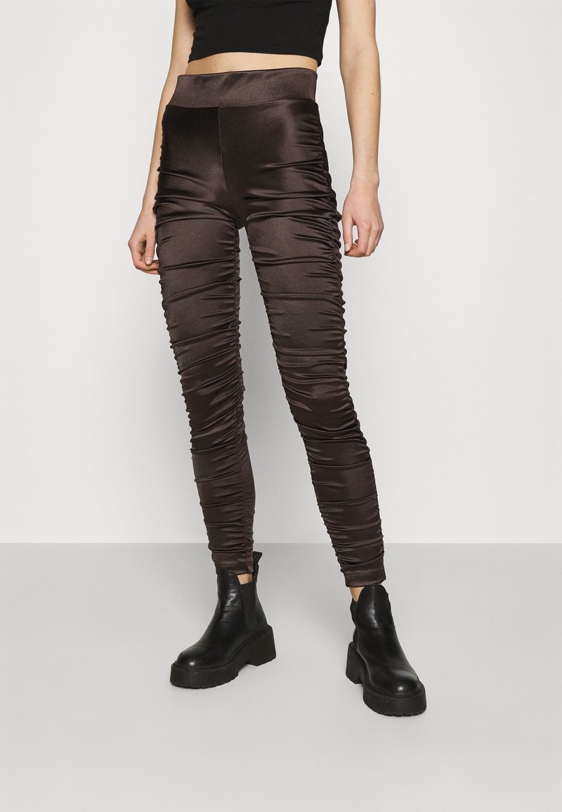 Leggings en satin marron avec un design froncé, une taille haute et une coupe ajustée. Associez-les à des bottines à plateforme noires pour un contraste.