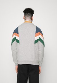 Grijze sweatshirt met meerkleurige hoekige strepen in marineblauw, groen, oranje en wit. Voorzien van een geribde kraag en manchetten.