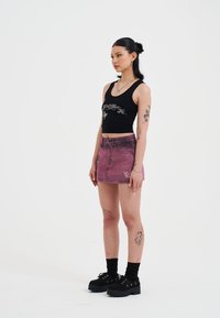 Zwarte cropped tanktop met zilveren graphic, gecombineerd met een vervaagde roze denimrok met borduursel. Zwarte chunky schoenen en zwarte sokken.