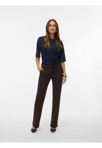 Temno modra kratka majica z naborki na strani, kombinirana s temno rjavimi krojenimi hlačami. Gladek tekstura, prilagojen kroj. Rjavi čevlji s koničastim prstom.