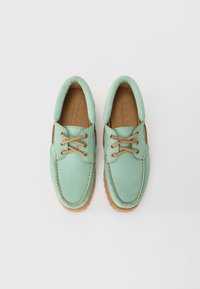 Šviesiai žalios spalvos odiniai batai su apvalia nosimi, rusvomis raištelėmis ir tekstūruotu padu; pasižymi siuvimu ir paminkštintu apykaklėle.