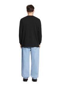 Czarna koszula z długim rękawem zestawiona z jasnoniebieskimi luźnymi dżinsami, charakteryzującymi się swobodnym krojem i minimalnymi detalami. Czarny obuwie dopełnia całość.