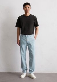 Czarna bawełniana koszulka w połączeniu z jasnoniebieskimi zwężającymi się dżinsami, z zapięciem na guziki z przodu, oraz białymi trampkami. Prosty, nowoczesny design.