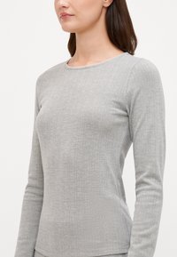 Haut gris à manches longues avec texture côtelée et encolure festonnée. Fabriqué en tissu doux, avec un design ajusté et une coupe droite à l'ourlet.