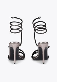 Sandały na obcasie w metalicznej srebrze z czarnymi spiralnymi paskami. Otwarty czubek, eleganckie, smukłe obcasy oraz teksturowane detale na paskach.