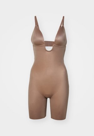 Body aderente di colore marrone chiaro, morbido al tatto, con scollatura a V profonda e spalline regolabili. Presenta una parte frontale con taglio e una lunghezza corta delle gambe per garantire comfort.