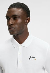 Vit pikétröja med klassisk krage, texturerad fabric och treknapplikning. Dekorerad med "BOSS"-logotypen och små accenter.