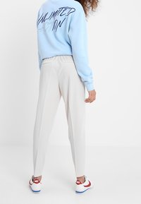 Jasnoniebieska bluza z napisem "UNLIMITED ACTION" na plecach, w połączeniu z zwężającymi się białymi spodniami i czerwono-białymi sneakersami Nike.