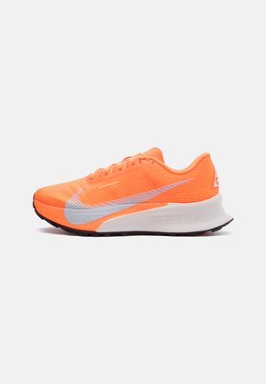 Lyst oransje løpesko med grå Nike-swoosh, hvit dempet såle og svart yttersåle, vist fra siden på en ensfarget bakgrunn.